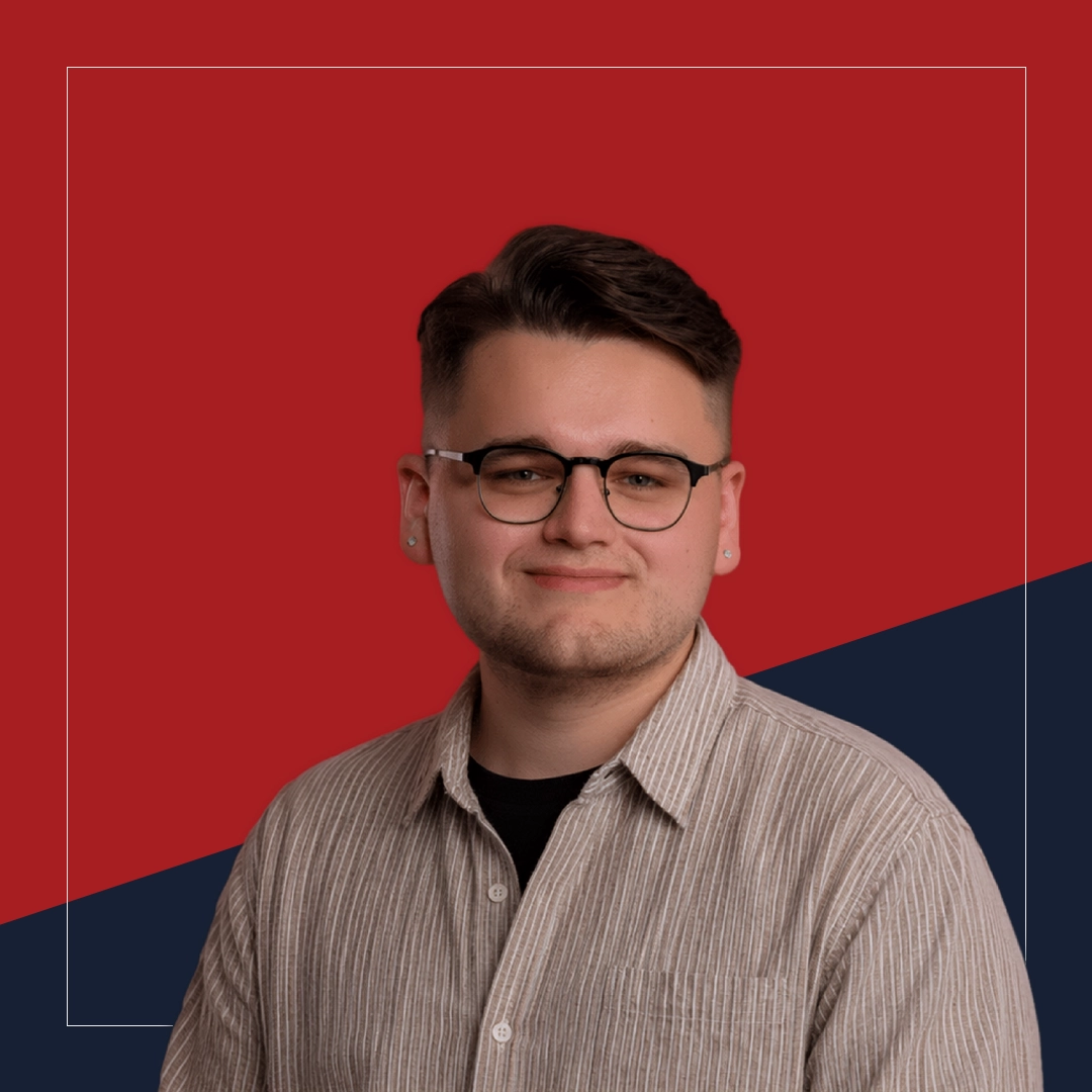 Portrait of Owen Denesuik smiling at the camera with a red and navy background.